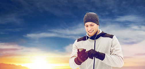 Image showing happy man with earphones and smartphone in winter