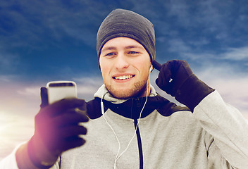 Image showing happy man with earphones and smartphone in winter