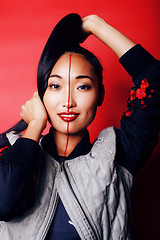 Image showing young pretty asian girl posing cheerful on red background, fashion style makeup and hair, lifestyle modern orient people concept