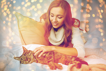 Image showing happy young woman with cat lying in bed at home