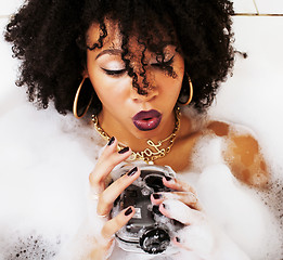 Image showing young afro-american teen girl laying in bath with foam, wearing 