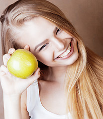 Image showing young pretty blond woman with green apple happy cheerful smiling close up on warm brown background, lifestyle real people concept