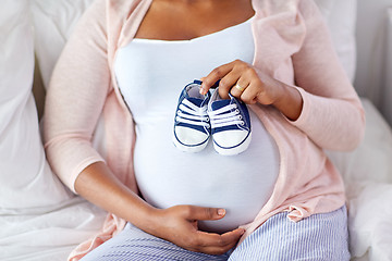 Image showing pregnant african woman with baby bootees in bed