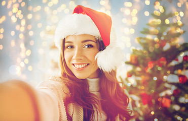 Image showing happy woman in santa hat over christmas tree