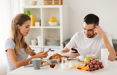 Image showing couple with smartphones having breakfast at home