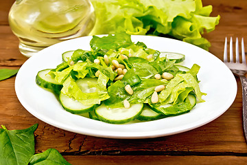 Image showing Salad from spinach and cucumber with cedar nuts on board