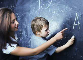 Image showing little cute boy in glasses with young real teacher, classroom studying at blackboard school