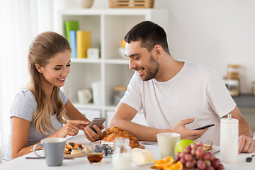 Image showing couple with smartphones having breakfast at home