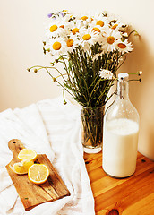 Image showing Simply stylish wooden kitchen with bottle of milk and glass on table, summer flowers camomile, healthy food moring concept