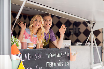 Image showing happy young sellers waving hands at food truck