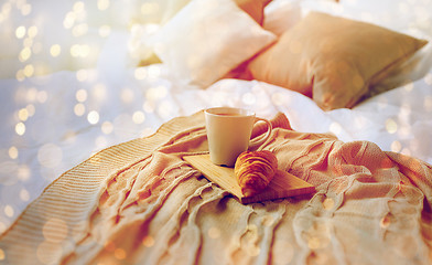 Image showing coffee cup and croissant on plaid in bed at home