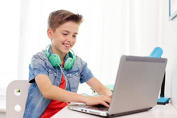 Image showing happy boy with headphones typing on laptop at home