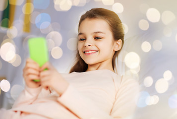Image showing happy girl in bed with smartphone over lights