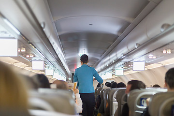 Image showing Interior of commercial airplane with stewardess serving passengers on seats during flight.