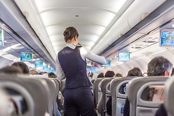 Image showing Interior of commercial airplane with stewardess serving passengers on seats during flight.