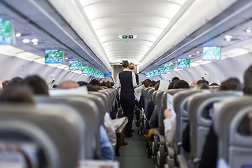 Image showing Interior of commercial airplane with stewardess serving passengers on seats during flight.