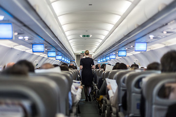 Image showing Interior of commercial airplane with stewardess serving passengers on seats during flight.