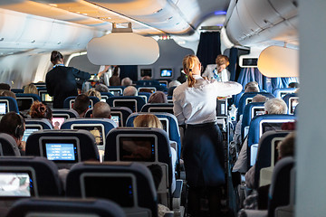 Image showing Interior of large commercial airplane with stewardesses serving passengers on seats during flight.