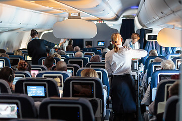 Image showing Interior of large commercial airplane with stewardesses serving passengers on seats during flight.