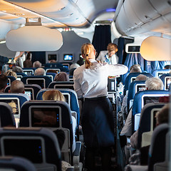 Image showing Interior of large commercial airplane with stewardesses serving passengers on seats during flight.