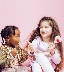 Image showing lifestyle people concept: diverse nation children playing together, caucasian girl with african little girl holding candy happy smiling close up on pink background