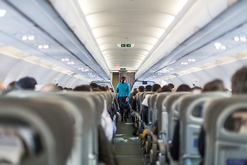 Image showing Interior of commercial airplane with stewardess serving passengers on seats during flight.