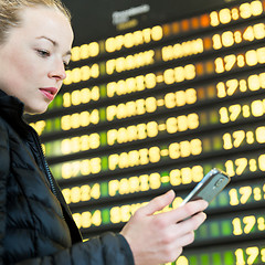 Image showing Woman at airport in front of flight information board checking her phone.