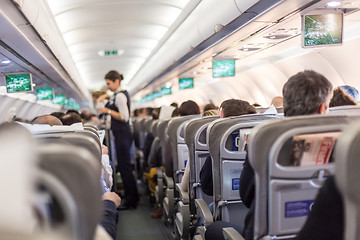 Image showing Interior of commercial airplane with stewardess serving passengers on seats during flight.