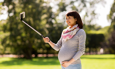 Image showing happy pregnant asian woman taking selfie at park