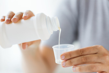 Image showing woman pouring syrup from bottle to medicine cup