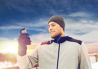 Image showing happy man with earphones and smartphone in winter