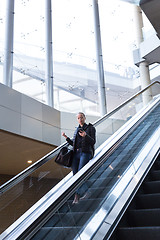 Image showing Businesswoman with large black bag and mobile phone descending on escalator.