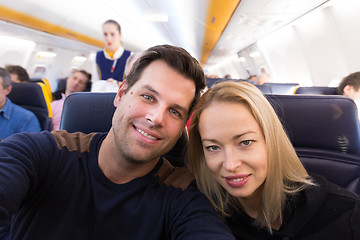 Image showing Young handsome couple taking a selfie on commercial airplane.