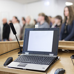 Image showing Laptop and microphone on the rostrum in lecture hall full of conference participants.