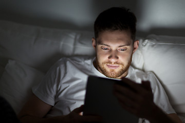 Image showing young man with tablet pc in bed at home bedroom