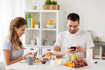 Image showing couple with smartphones having breakfast at home