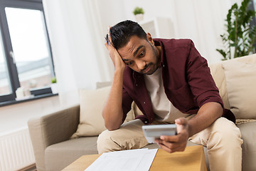 Image showing confused man with papers and calculator at home