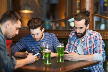 Image showing friends with smartphones and green beer at pub