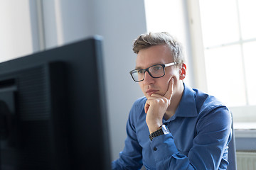 Image showing Casual businessman working in office, sitting at desk, typing on keyboard, looking at computer screen.