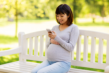 Image showing happy pregnant asian woman with smartphone at park