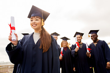 Image showing happy students in mortar boards with diplomas