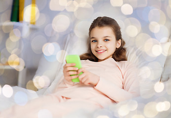 Image showing happy girl lying in bed with smartphone at home