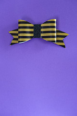 Image showing Black and golden striped bow tie over ultra violet background.
