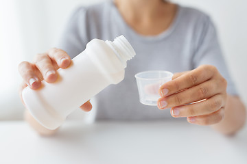 Image showing woman pouring syrup from bottle to medicine cup