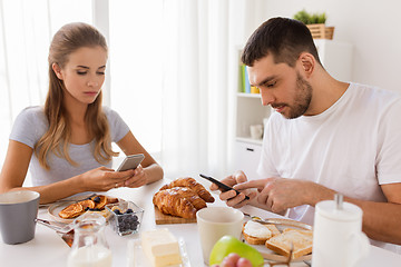 Image showing couple with smartphones having breakfast at home