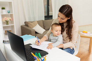 Image showing happy mother with baby and papers working at home