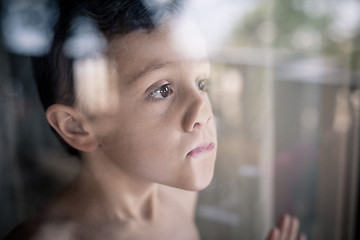 Image showing one sad little boy standing near the window at the day time.