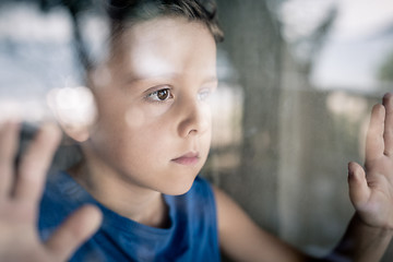 Image showing one sad little boy standing near the window at the day time.