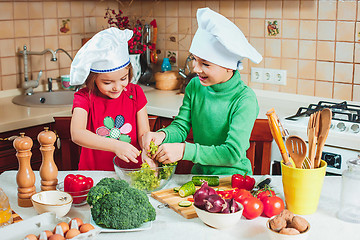 Image showing happy family funny kids are preparing the a fresh vegetable salad in the kitchen