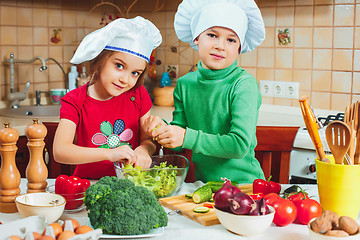 Image showing happy family funny kids are preparing the a fresh vegetable salad in the kitchen